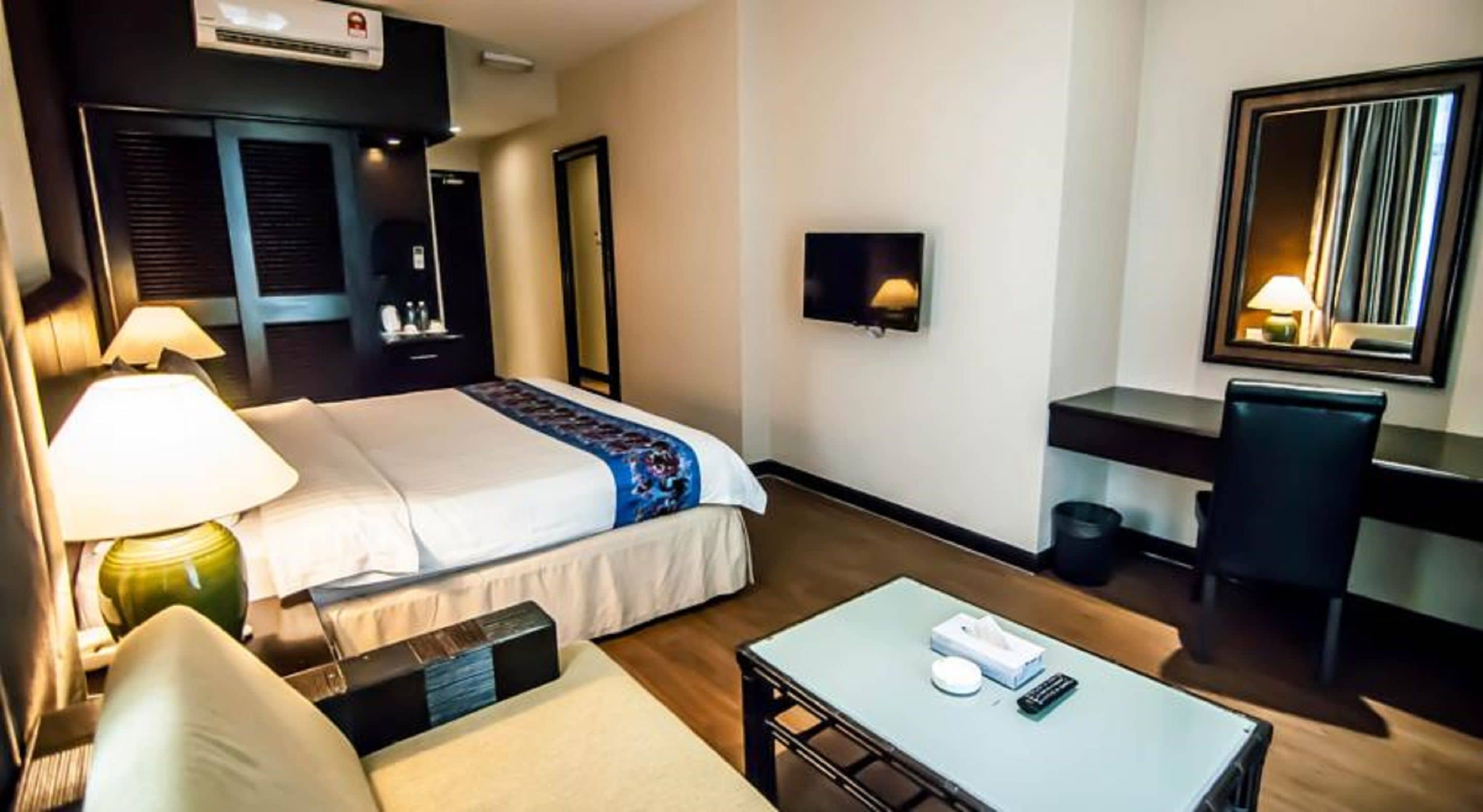 A hotel room with a bed, bedside table, lamp, desk, chair, and a TV.
