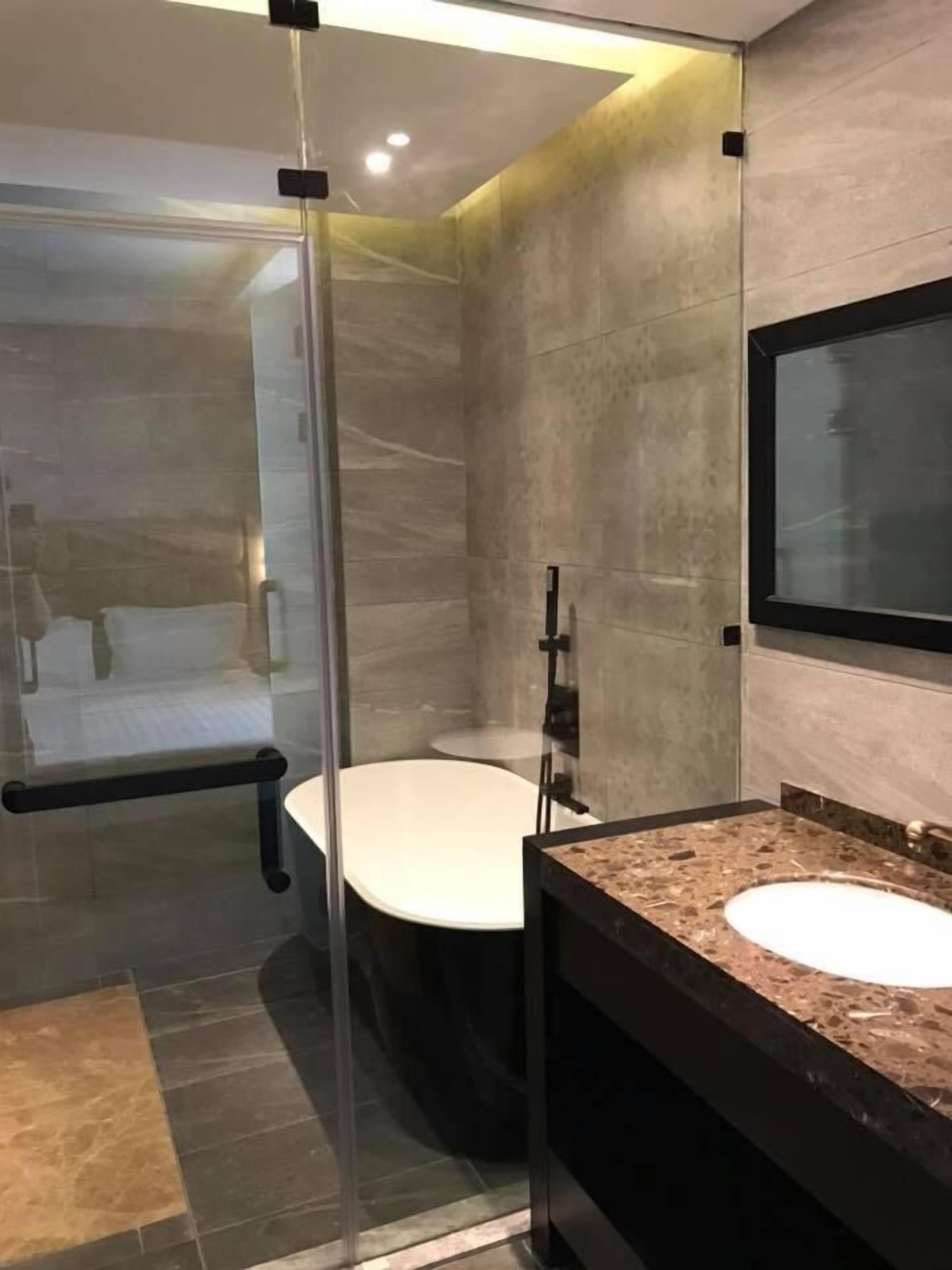 A modern bathroom with a glass shower enclosure, a freestanding bathtub, and a marble countertop sink.