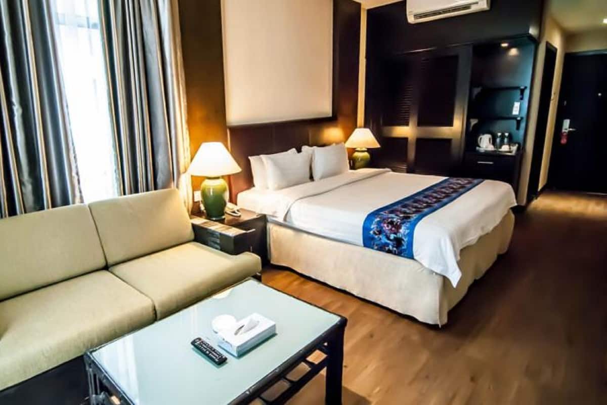 Ein Hotelzimmer mit einer Schlafcouch, einem Bett, einem Nachttisch mit Lampe und einem kleinen Tisch mit Fernbedienung.