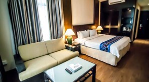 Una habitación de hotel con sofá, cama, mesita de noche con lámpara y una pequeña mesa con control remoto.