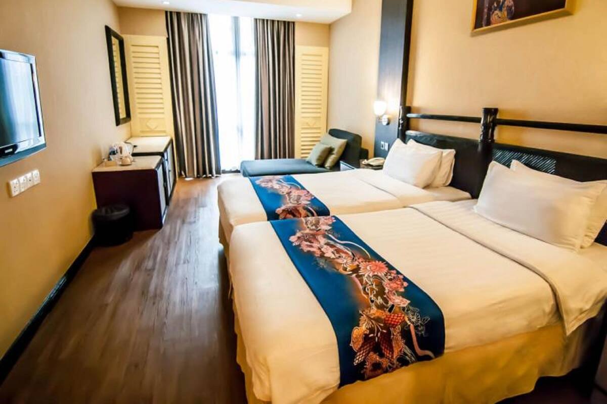 Ein Hotelzimmer mit zwei Betten, einem Schreibtisch, einem Sessel, einem Fernseher und einem großen Fenster mit Vorhängen.