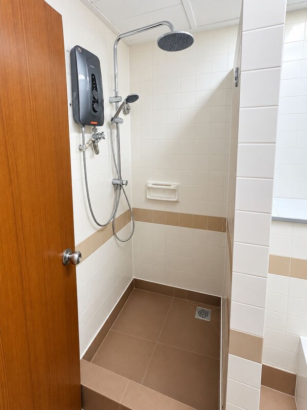 A bathroom with a shower, a soap dispenser, and a toilet.