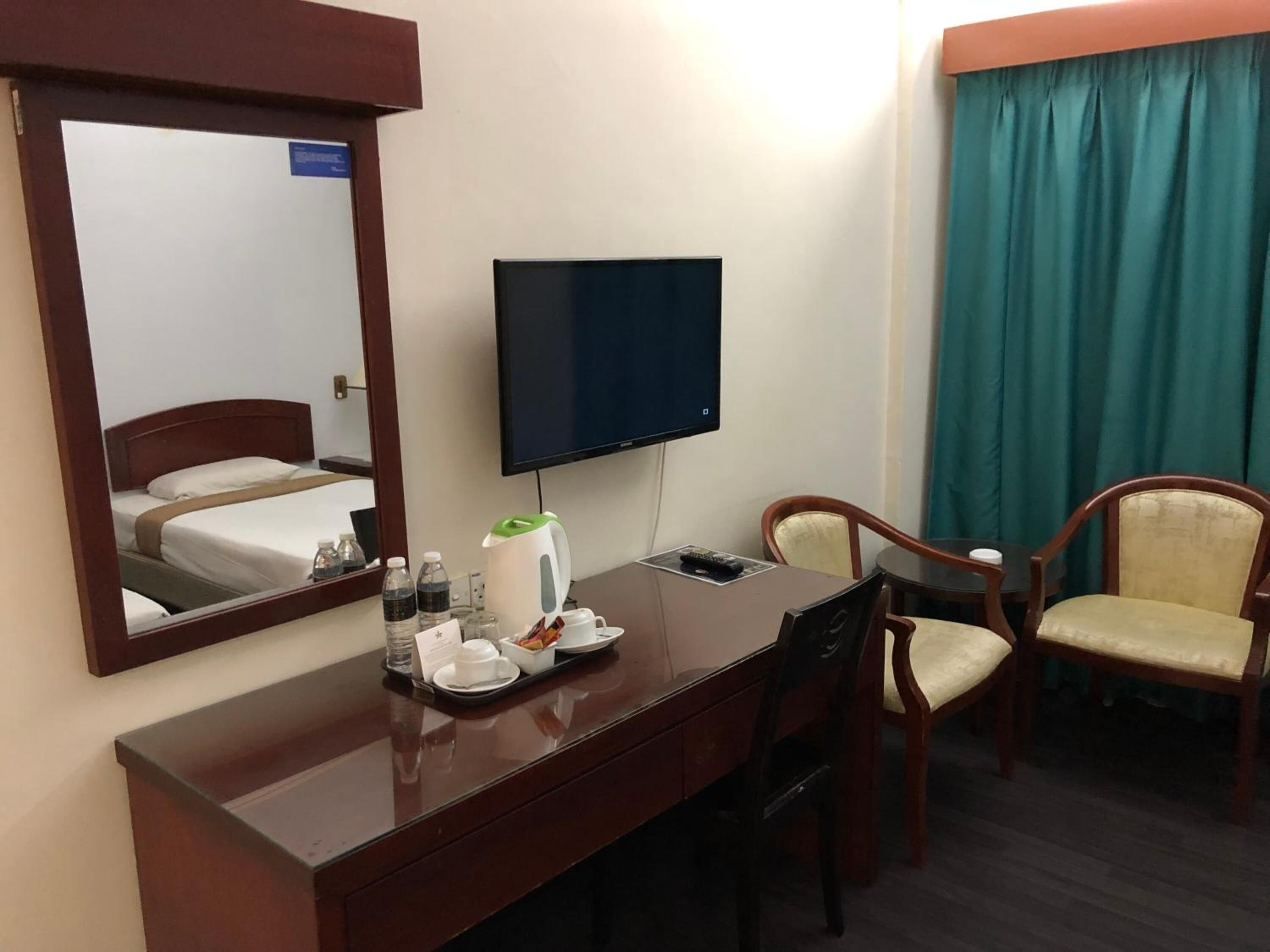 Ein Hotelzimmer mit einem Holztisch, einem Flachbildfernseher, einem Bett, einem Sessel und einem Fenster mit Vorhängen.