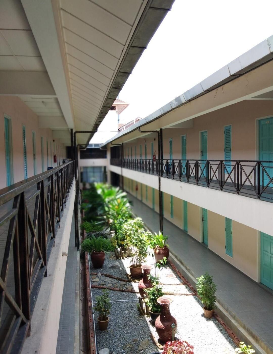 A covered corridor with potted plants and a metal railing.