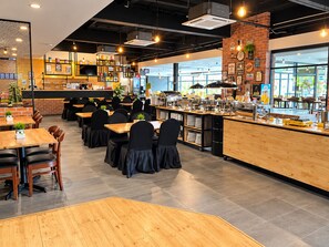 Ein modernes Café mit mehreren Tischen und Stühlen, einer Theke mit Speisen und einer Ziegelwand mit Kunstwerken.