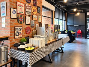 Montaje de bufé con mantel a cuadros, alimentos y una pared decorada con carteles antiguos.
