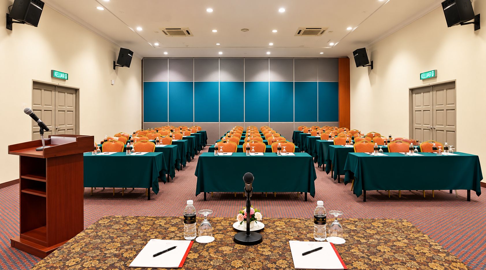 Un salón de conferencias con filas de mesas, sillas, un atril y un escenario.