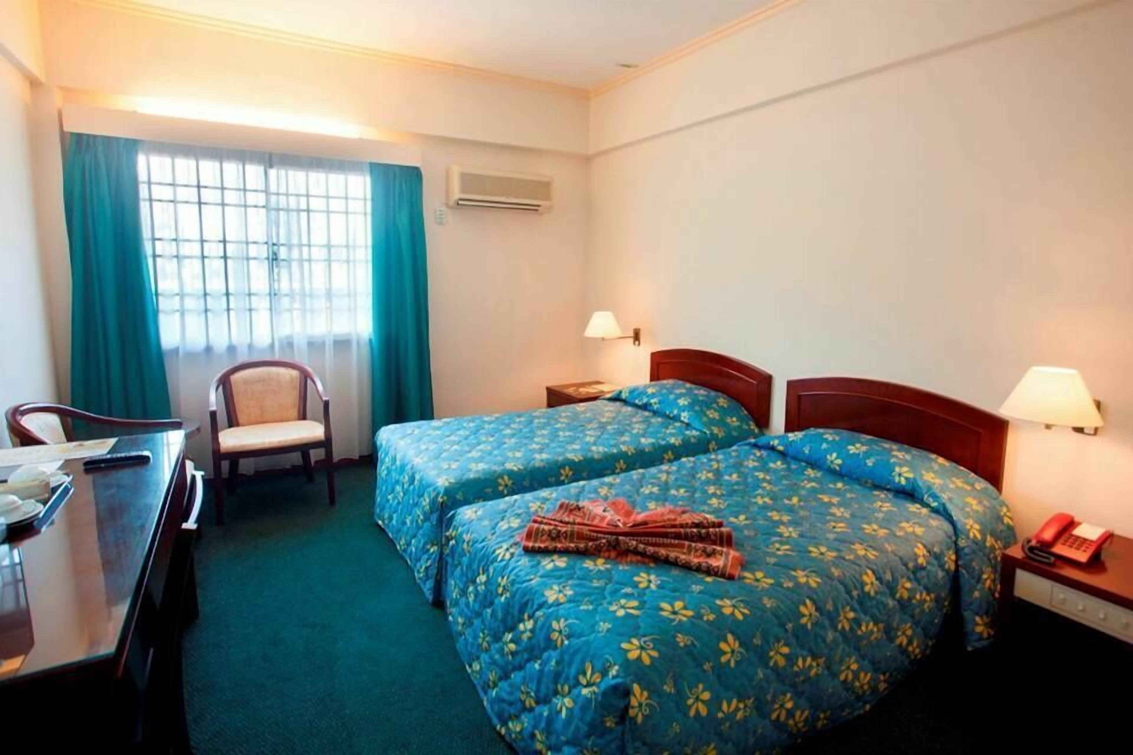 A hotel room with two beds, a desk, a chair, and a window with curtains.
