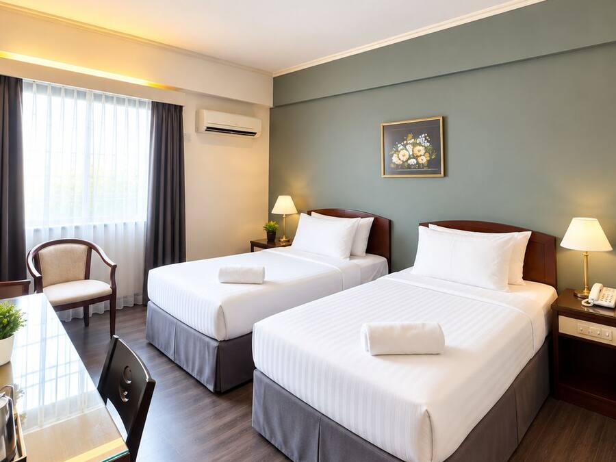 A hotel room with two beds, a desk, a chair, a lamp, and a painting on the wall.