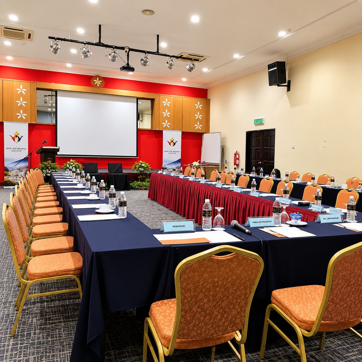 Ein Konferenzraum mit langem Tisch, Stühlen, Namensschildern und einer Projektionsleinwand.