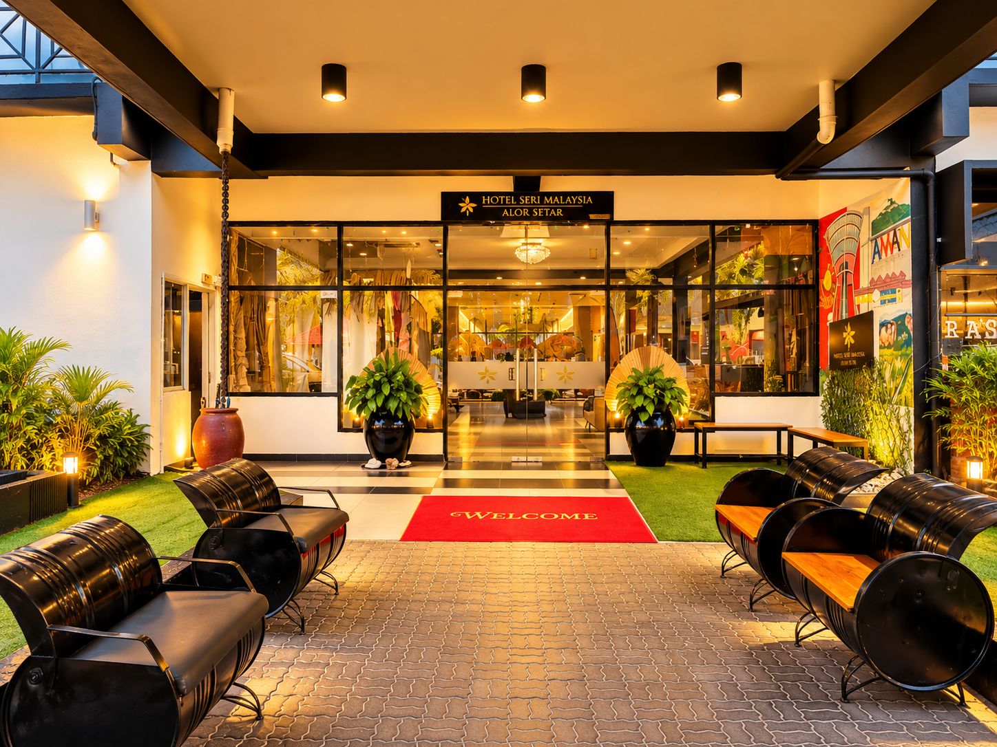 Een hotelentree met een rode loper, zitplaatsen buiten en een bord met Hotel Seri Malaysia Alor Setar.