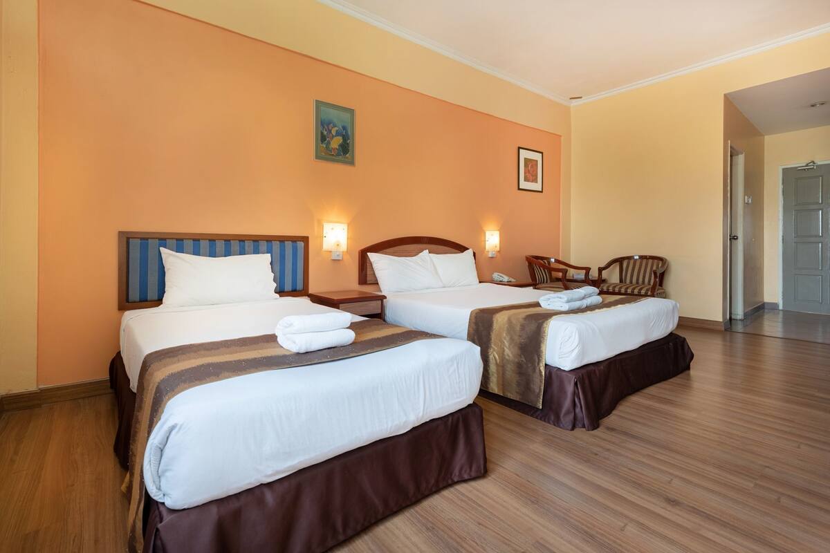 A hotel room with two beds, wooden flooring, and a door leading to a hallway.