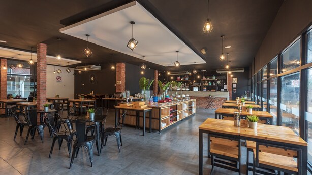 A modern cafe with wooden tables and chairs, a brick wall, and a large window. - Hotel Seri Malaysia Ipoh (Ipoh)