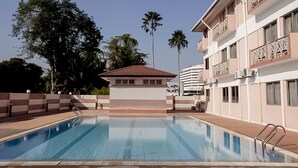 A swimming pool with a clear blue water surface, surrounded by a low brick wall and metal railings. In the background, there is a multi-story building with balconies and a palm tree. - Hotel Seri Malaysia Ipoh (Ipoh)