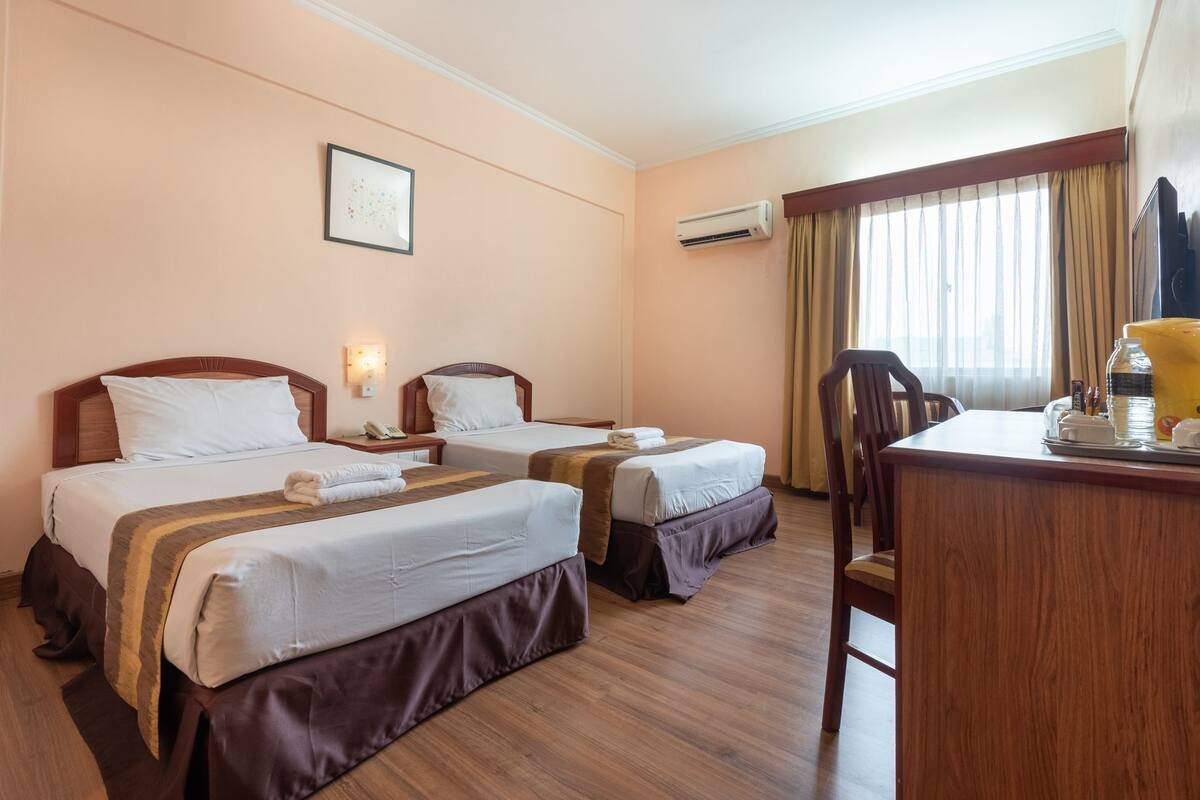 A hotel room with two beds, a desk, and a chair.