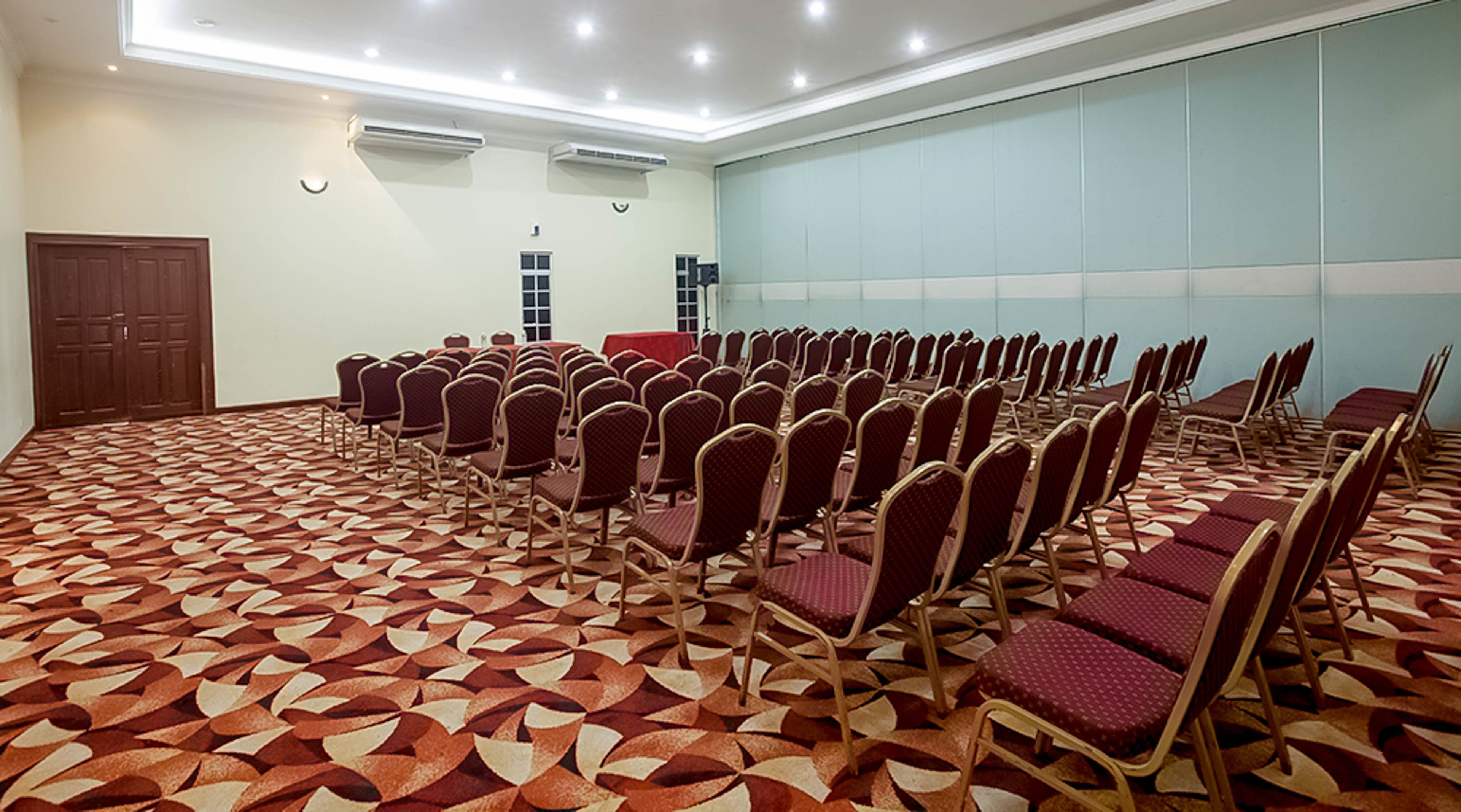 Una sala de conferencias con filas de sillas, una alfombra estampada y un ventanal grande.