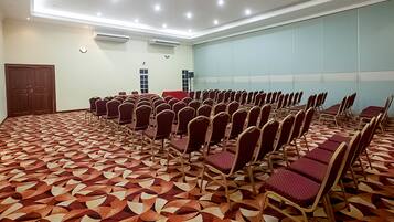 Una sala de conferencias con filas de sillas, una alfombra estampada y un ventanal grande.