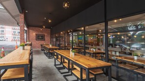 A restaurant with long wooden tables and benches, brick walls, and large windows. - Hotel Seri Malaysia Ipoh (Ipoh)