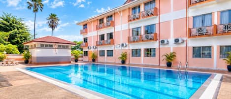 Un hotel con piscina, varios balcones y un pequeño edificio de techo rojo.