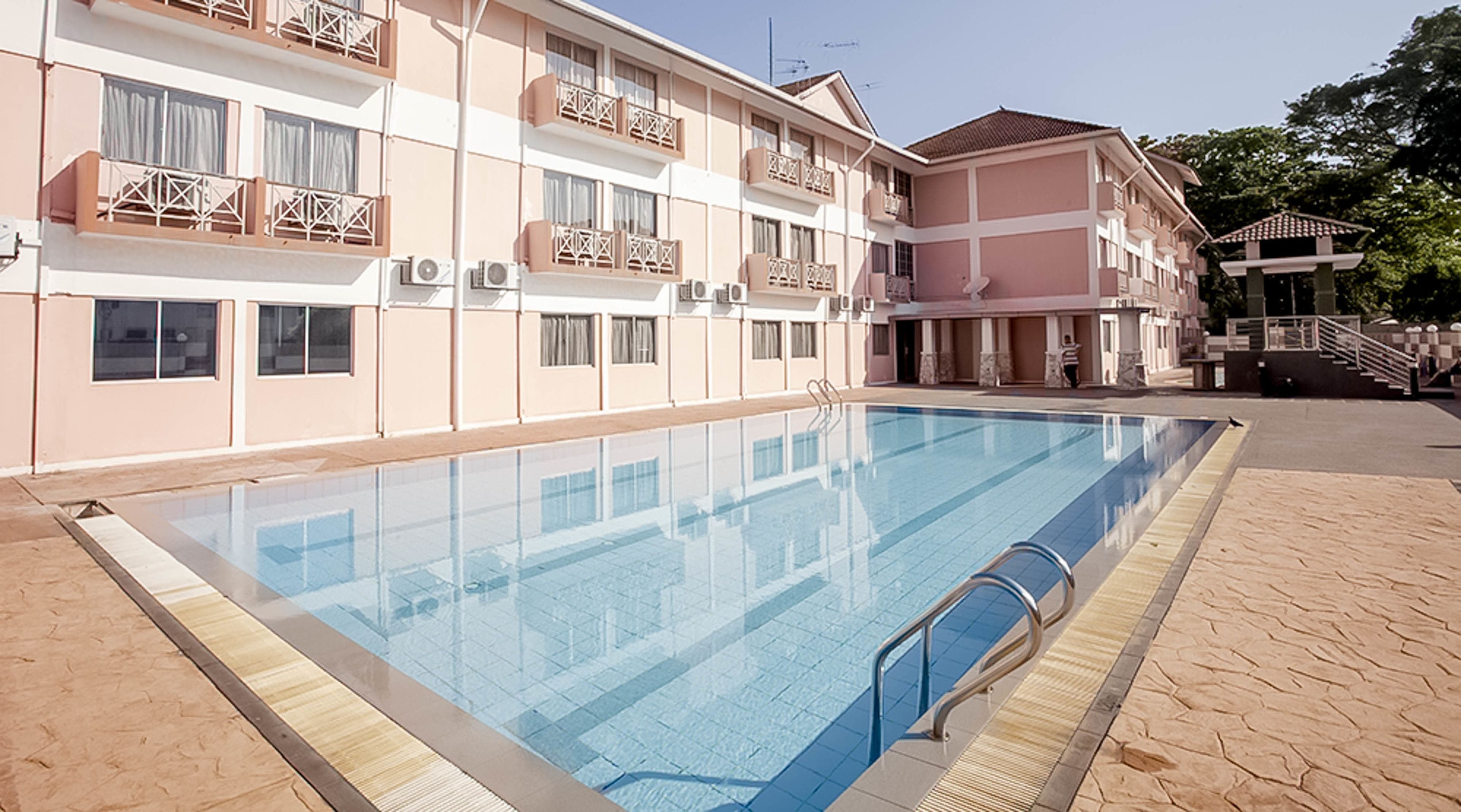 A swimming pool adjacent to a multi-story hotel with balconies and air conditioning units.
