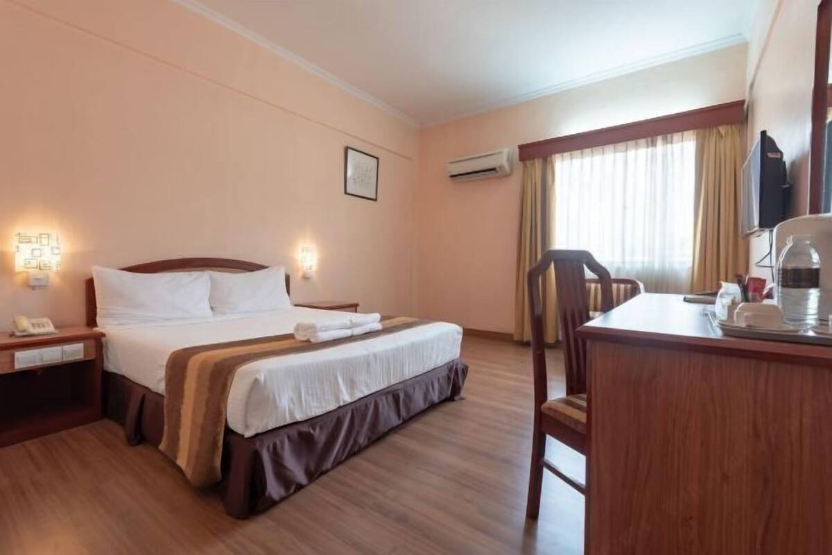 A hotel room with a bed, bedside table, lamp, and a desk with a chair.