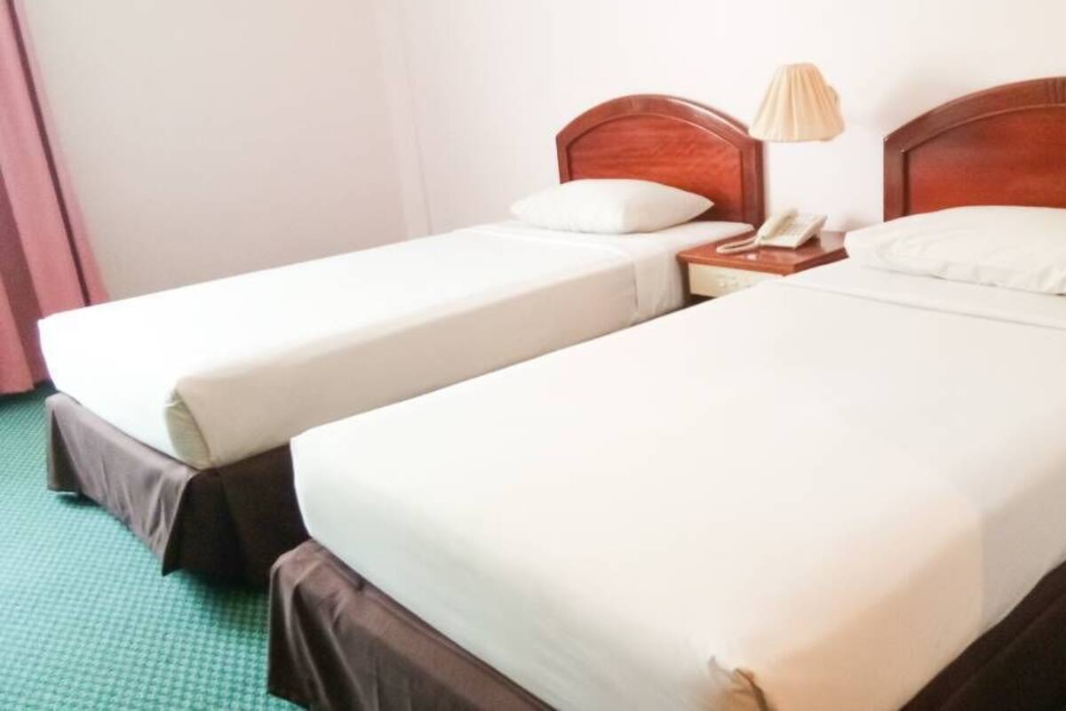 A hotel room with two single beds, each with a wooden headboard, white bedding, and a bedside lamp.
