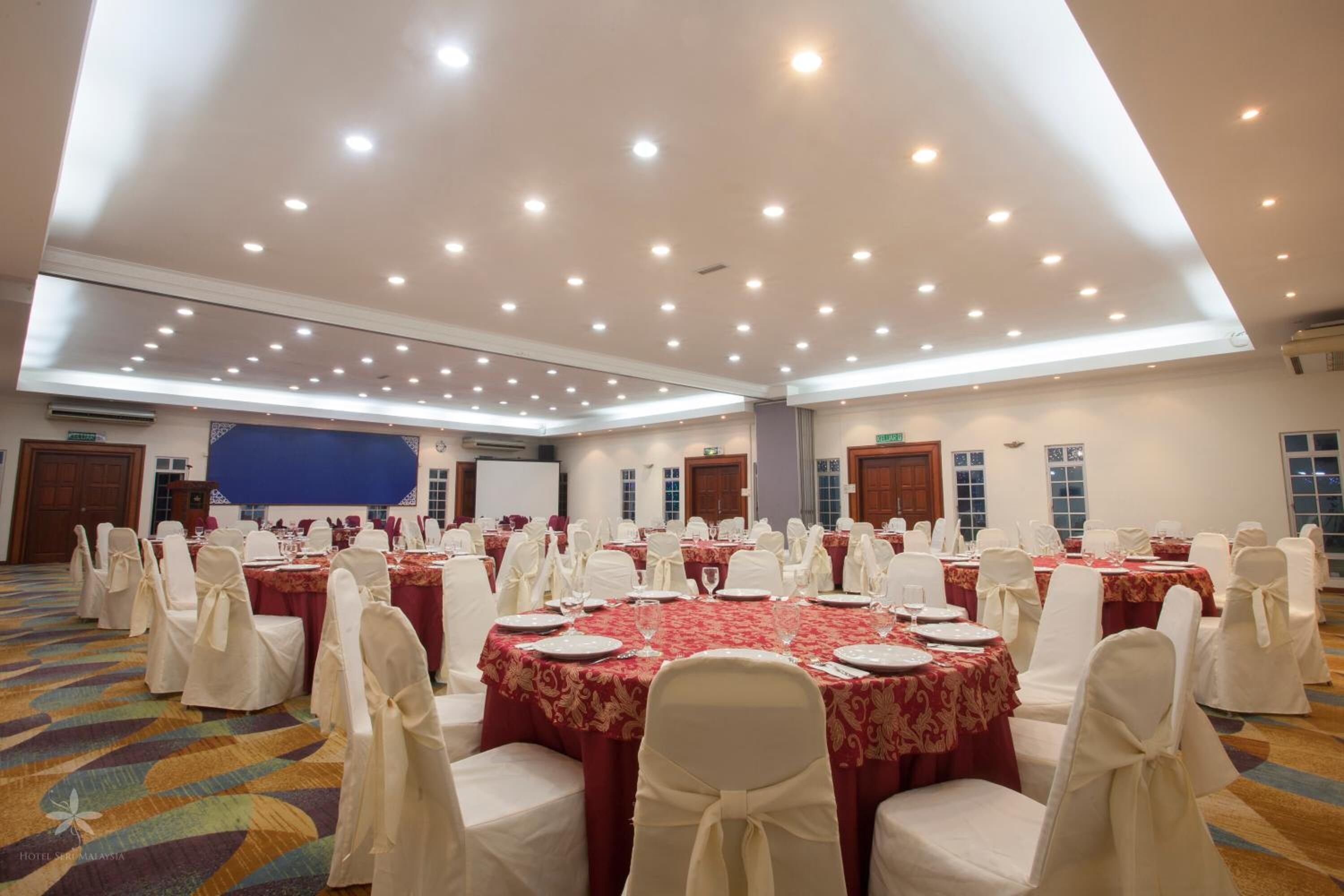A conference room with round tables, white chairs, and red tablecloths.