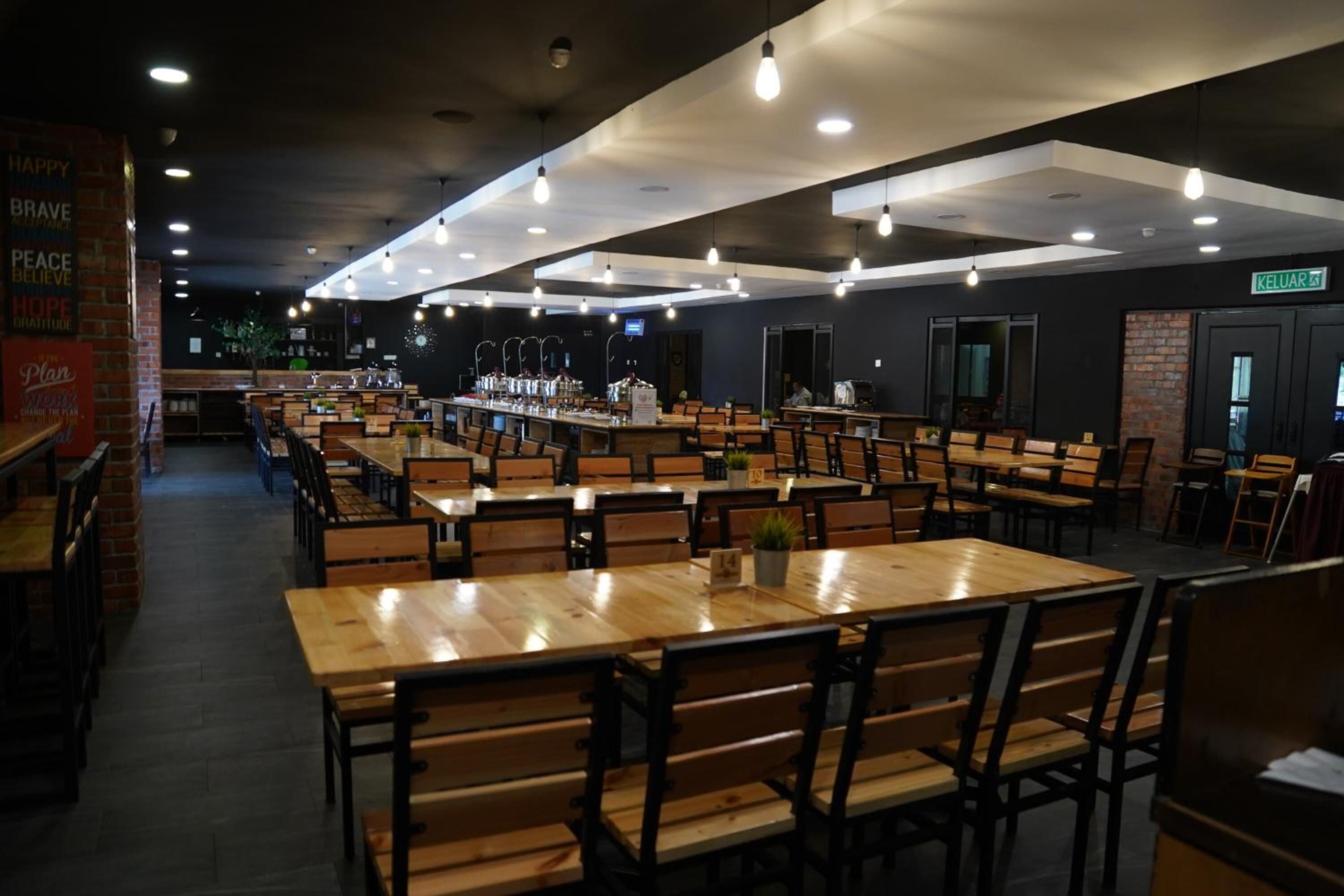 Ein geräumiges Restaurant mit mehreren Holztischen und Stühlen, einer Bar und einer Wand mit Ziegeln, verziert mit motivierenden Zitaten.