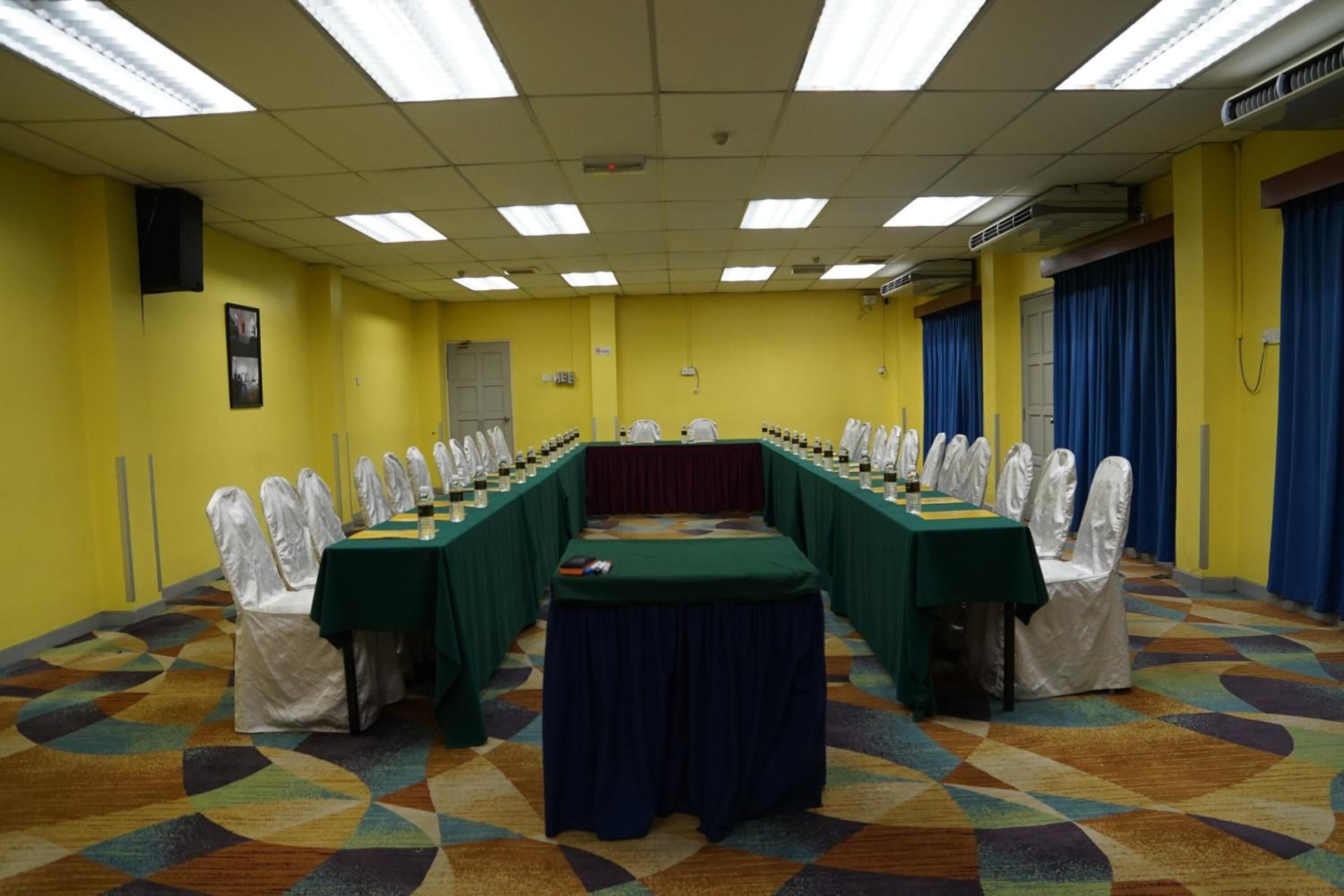 A conference room with a long table, white chairs, and a patterned carpet.