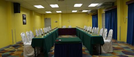A conference room with a long table, white chairs, and a patterned carpet.