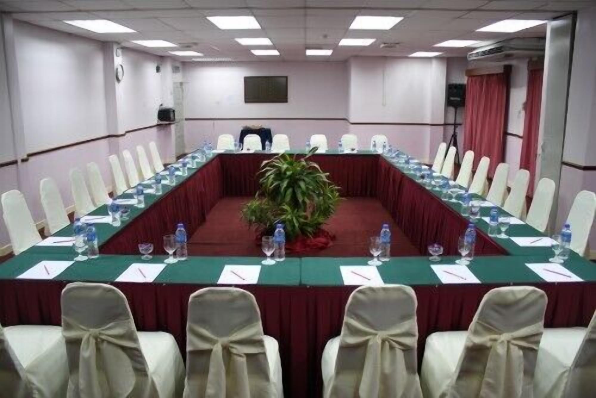 A conference room with a long table, white chairs, and a potted plant.