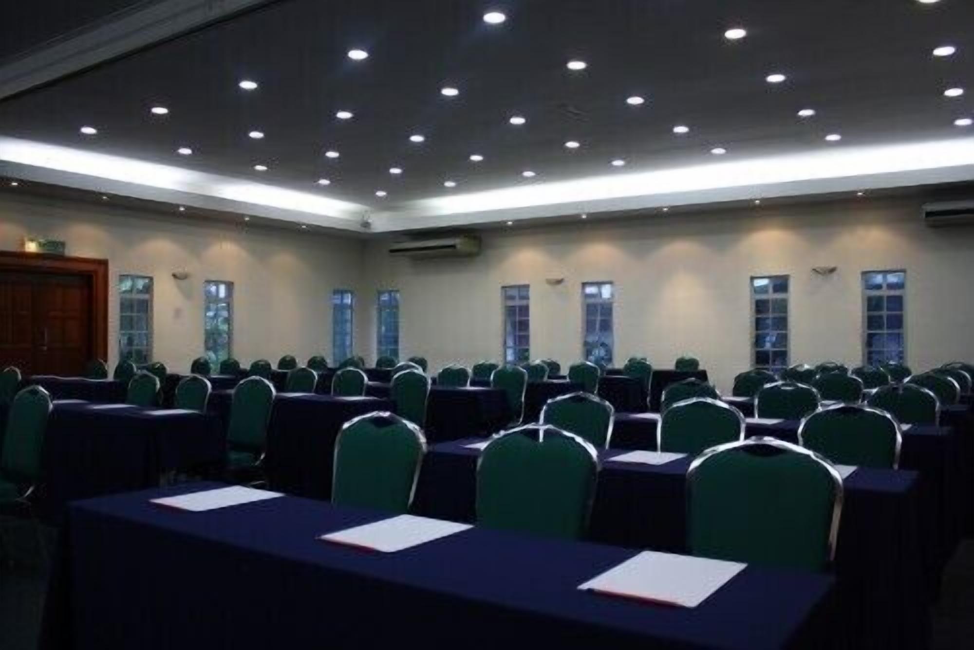 A conference room with rows of tables and chairs, air conditioning units, and windows.