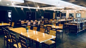 Un amplio comedor con varias mesas y sillas, una barra central con exhibición de alimentos e iluminación colgante.