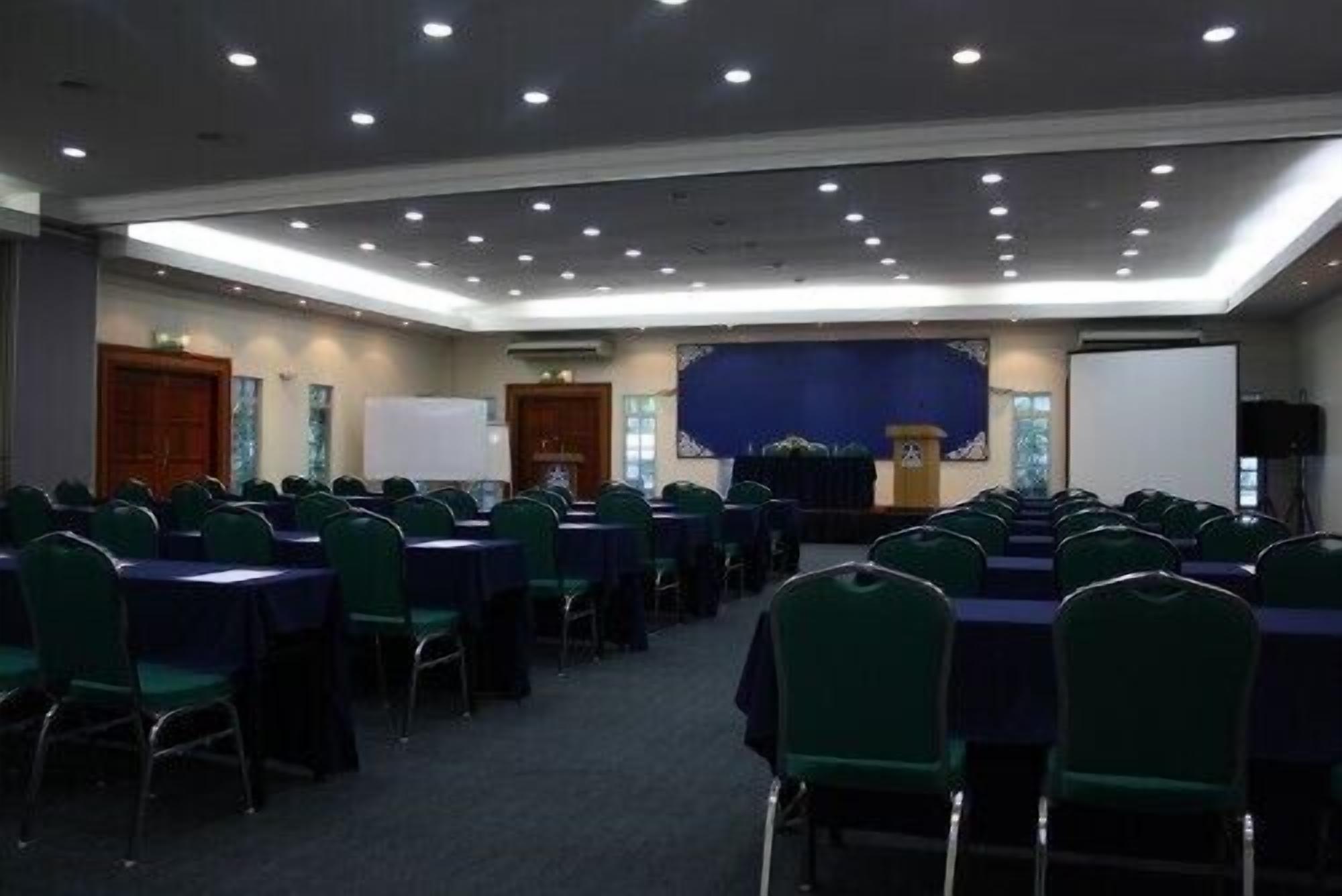 A conference room with rows of green chairs and tables, a stage with a podium, and a whiteboard.