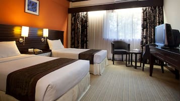 Habitación de hotel con dos camas, un escritorio, televisión, una silla y una ventana con cortinas.