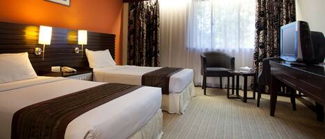 A hotel room with two beds, a desk with a television, a chair, and a window with curtains.