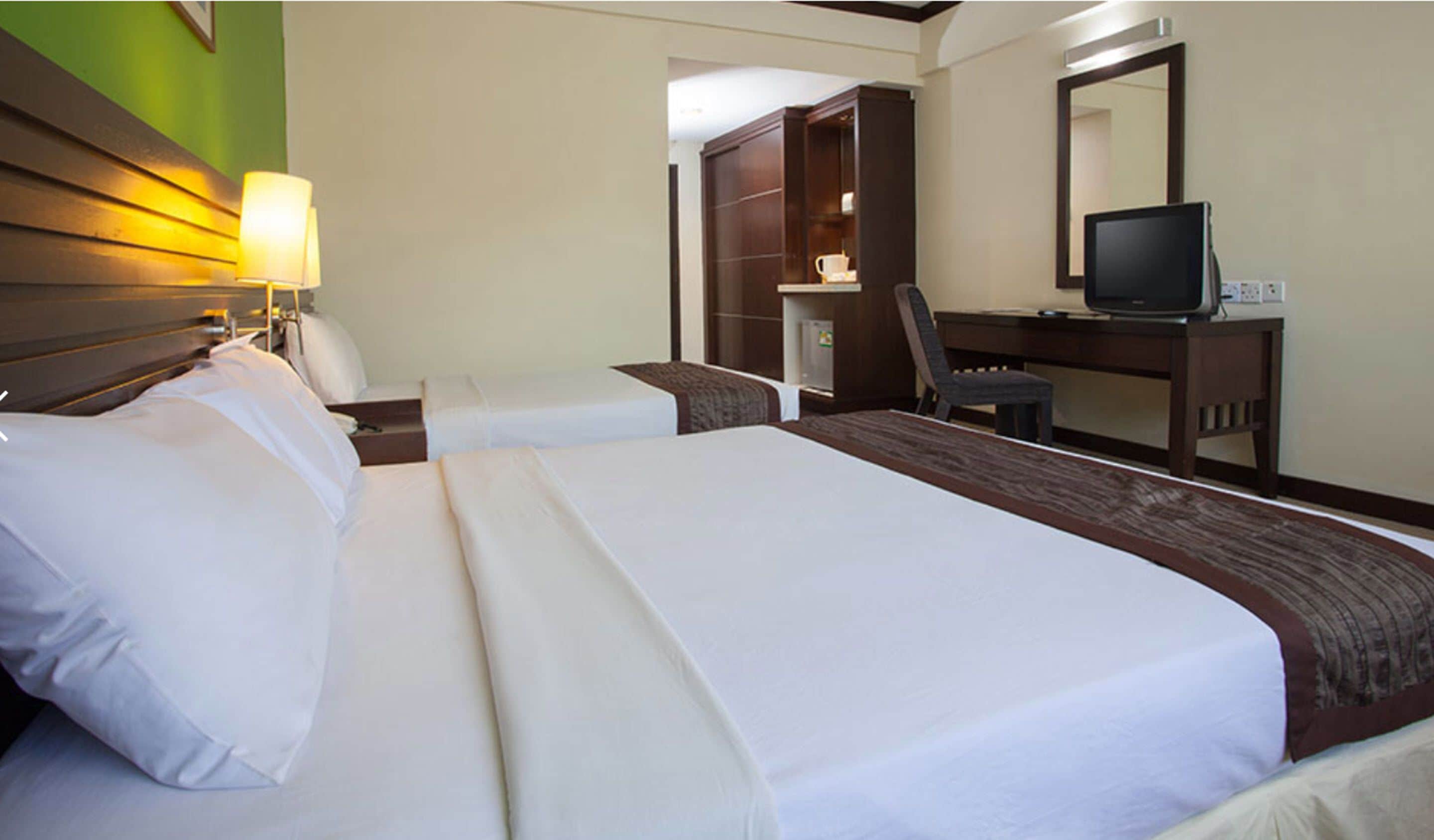 A hotel room with two beds, a desk with a television, a chair, and a wardrobe.