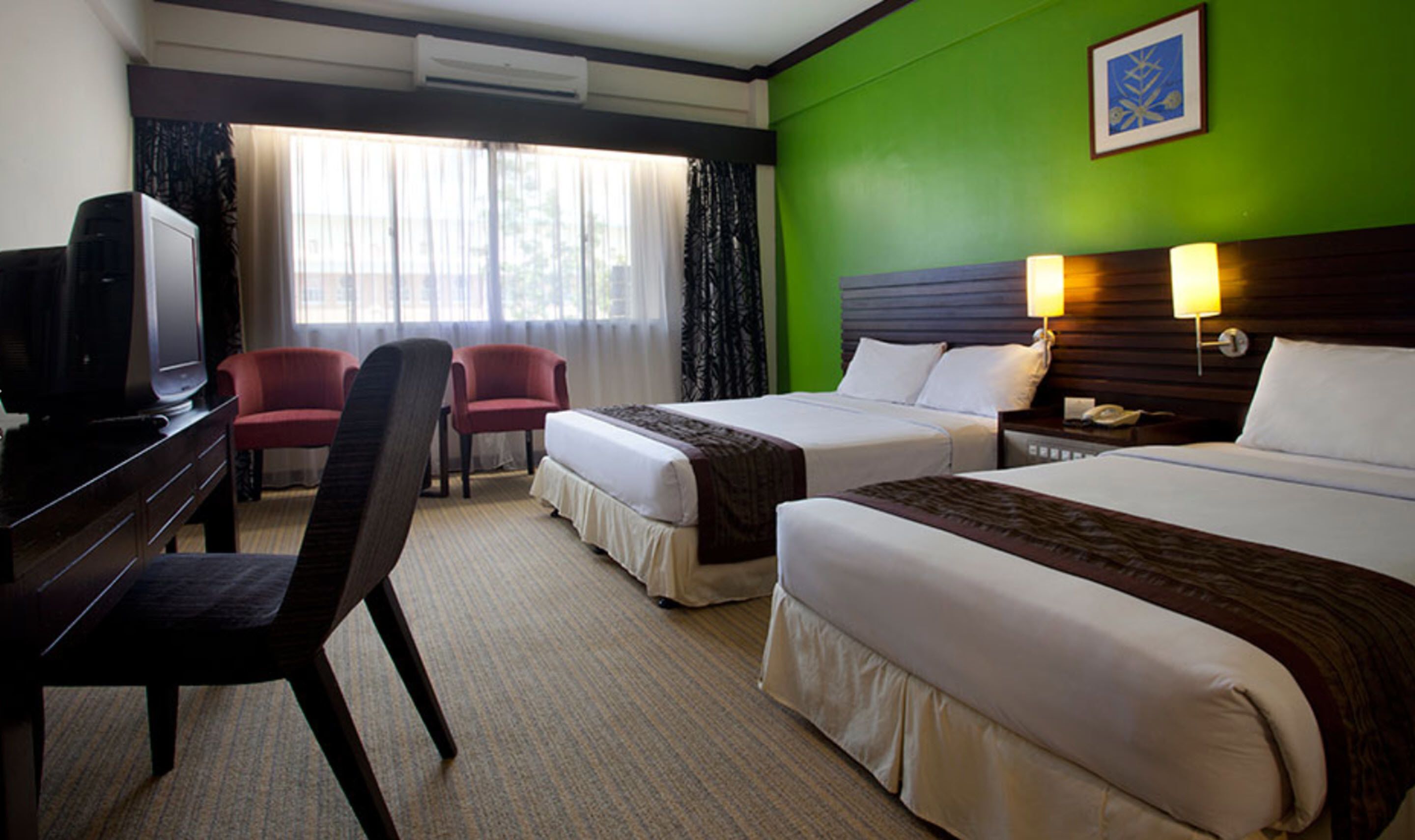A hotel room with two beds, a desk with a television, a chair, and a window with curtains.