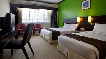 Ein Hotelzimmer mit zwei Betten, einem Schreibtisch, einem Fernseher, einem Sessel und einem Fenster mit Vorhängen.