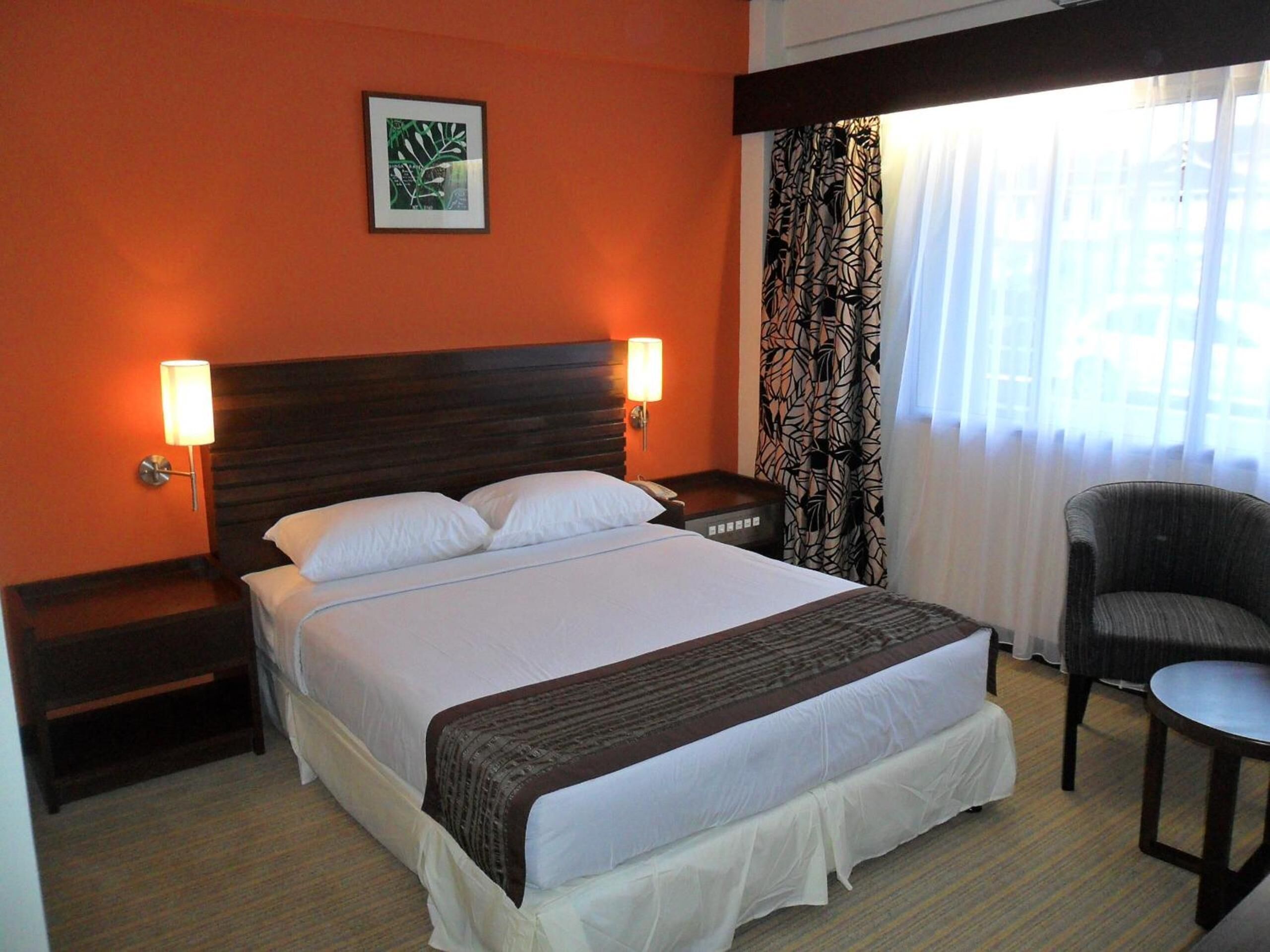 Habitación de hotel con una cama grande, dos lámparas de noche, una silla y una ventana con cortinas.