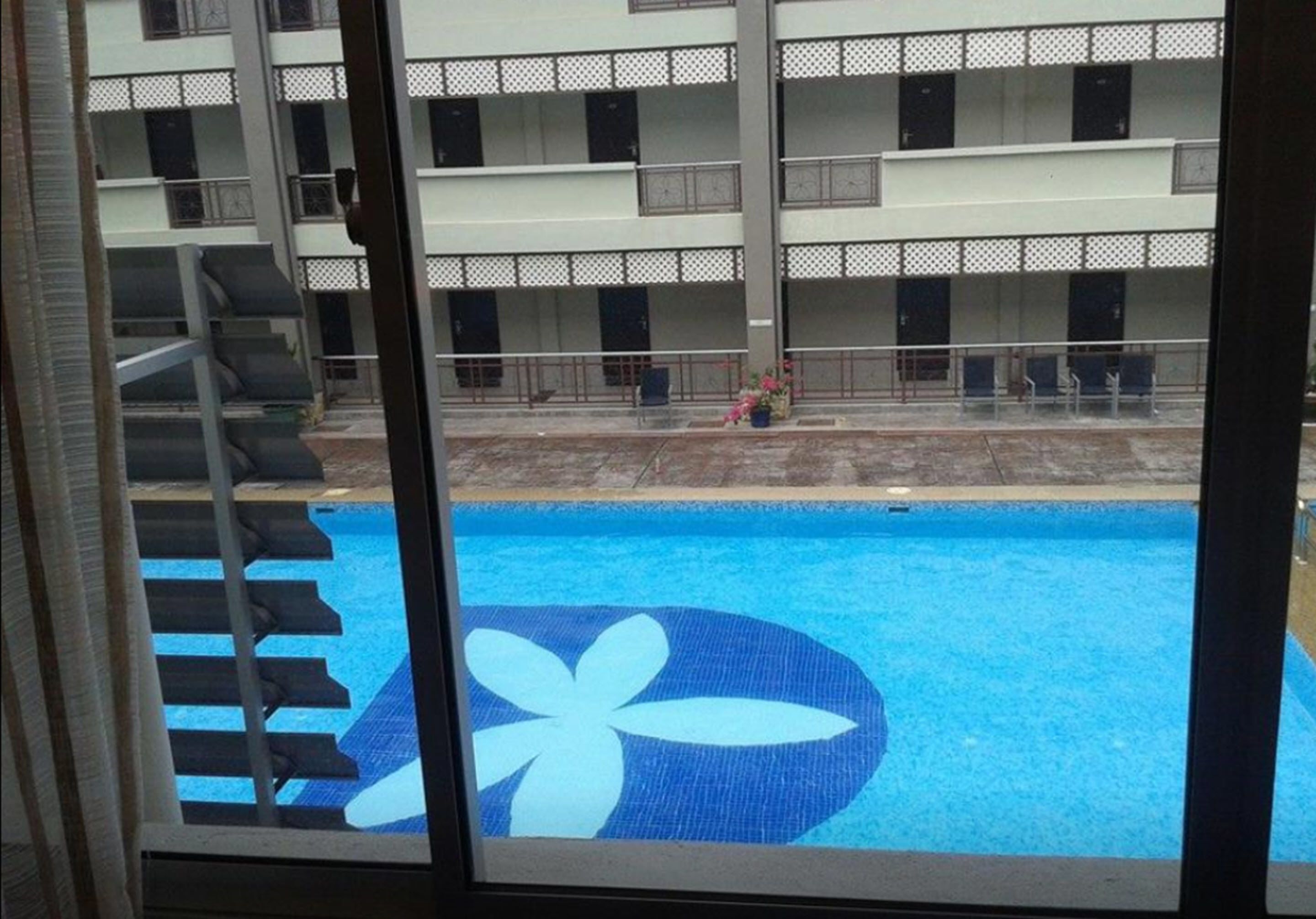 Une piscine aux motifs bleus et blancs, entourée d’un bâtiment doté de balcons et d’une clôture.