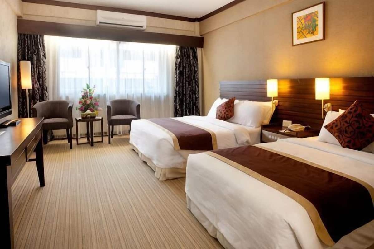 Een hotelkamer met twee bedden, een bureau, een stoel, een kleine tafel met een vaas en een televisie.