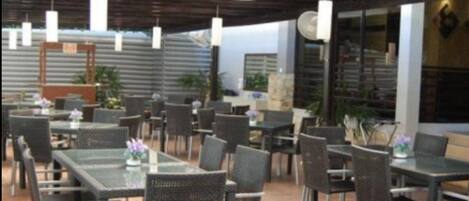Un área de comedor al aire libre con mesas y sillas, algunas decoradas con plantas.