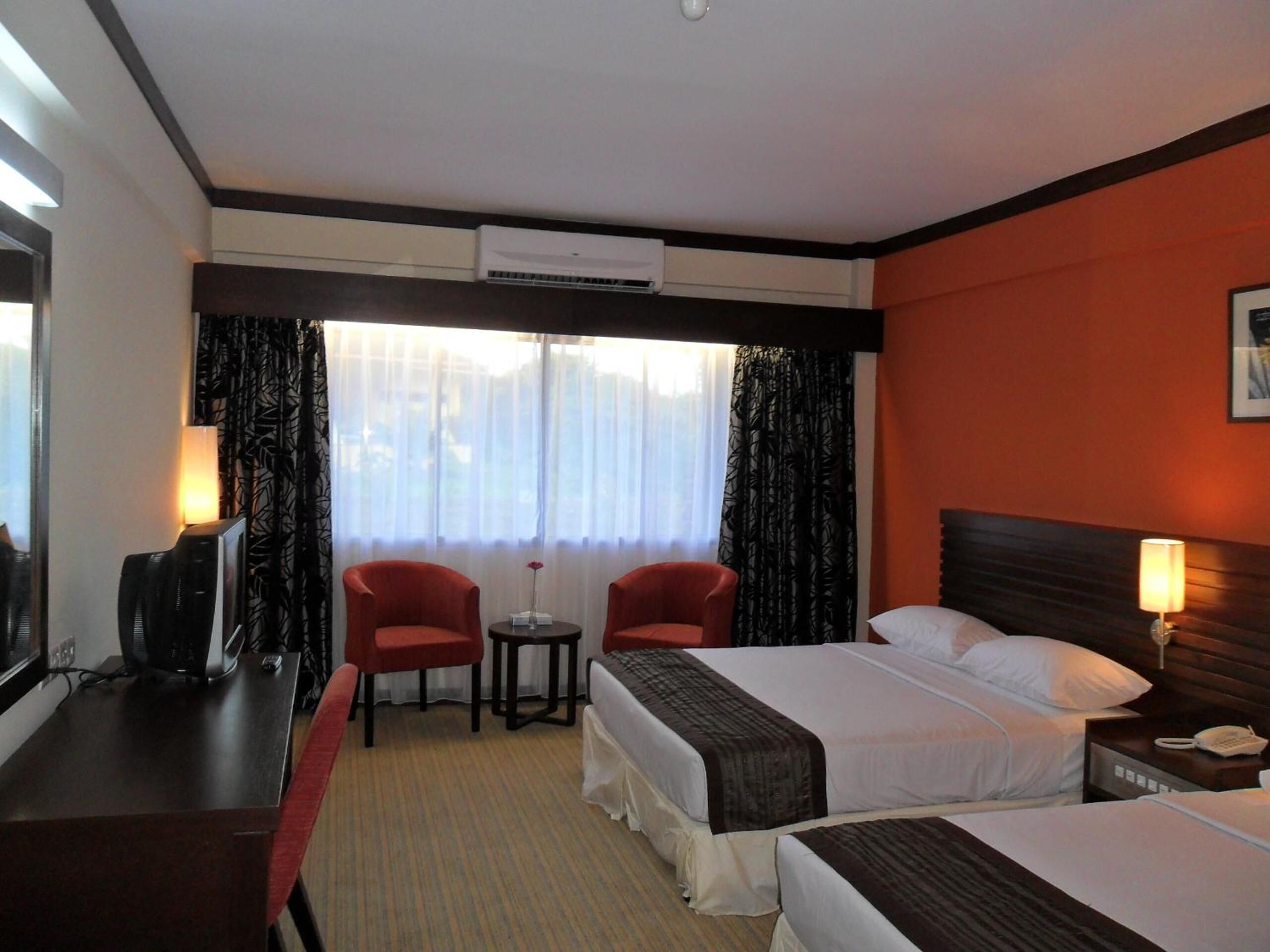 A hotel room with two beds, a desk, a chair, and a small table.