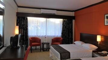 A hotel room with two beds, a desk, a chair, and a small table.