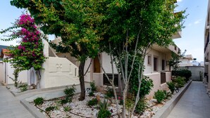 A courtyard with a white building, a tree, and a pink flowering plant. - Eleonora Anissaras (Hersonissos)