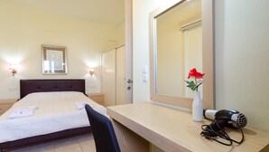 A hotel room with a bed, bedside table, mirror, and a red flower vase. - Eleonora Anissaras (Hersonissos)