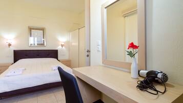 Een hotelkamer met een bed, nachtkastje, spiegel en een rode bloevas.