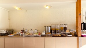 A buffet setup with various food items and beverages, including a coffee machine, a fruit bowl, and a juice dispenser. - Eleonora Anissaras (Hersonissos)