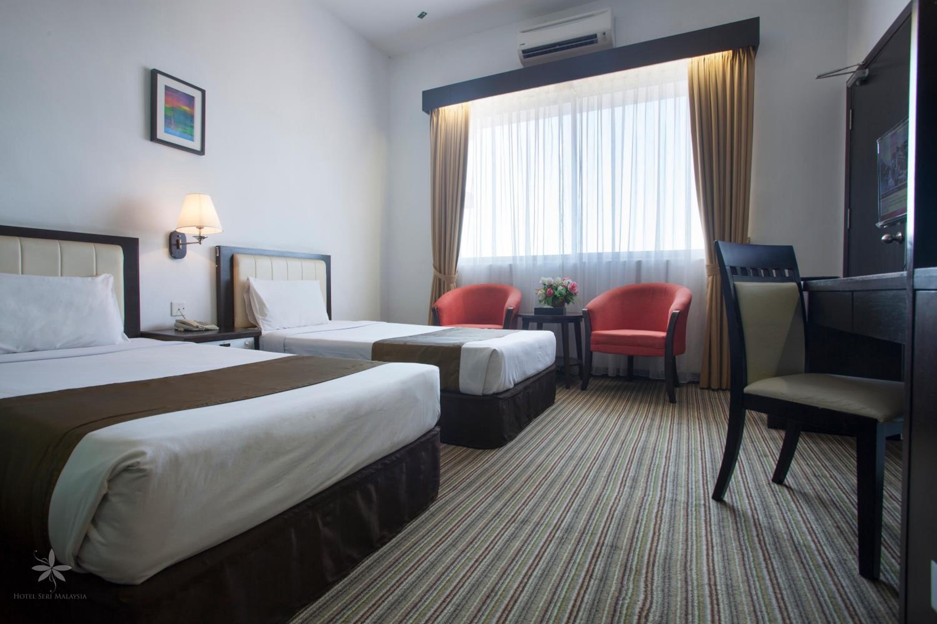 A hotel room with two beds, a desk, a chair, and a TV.